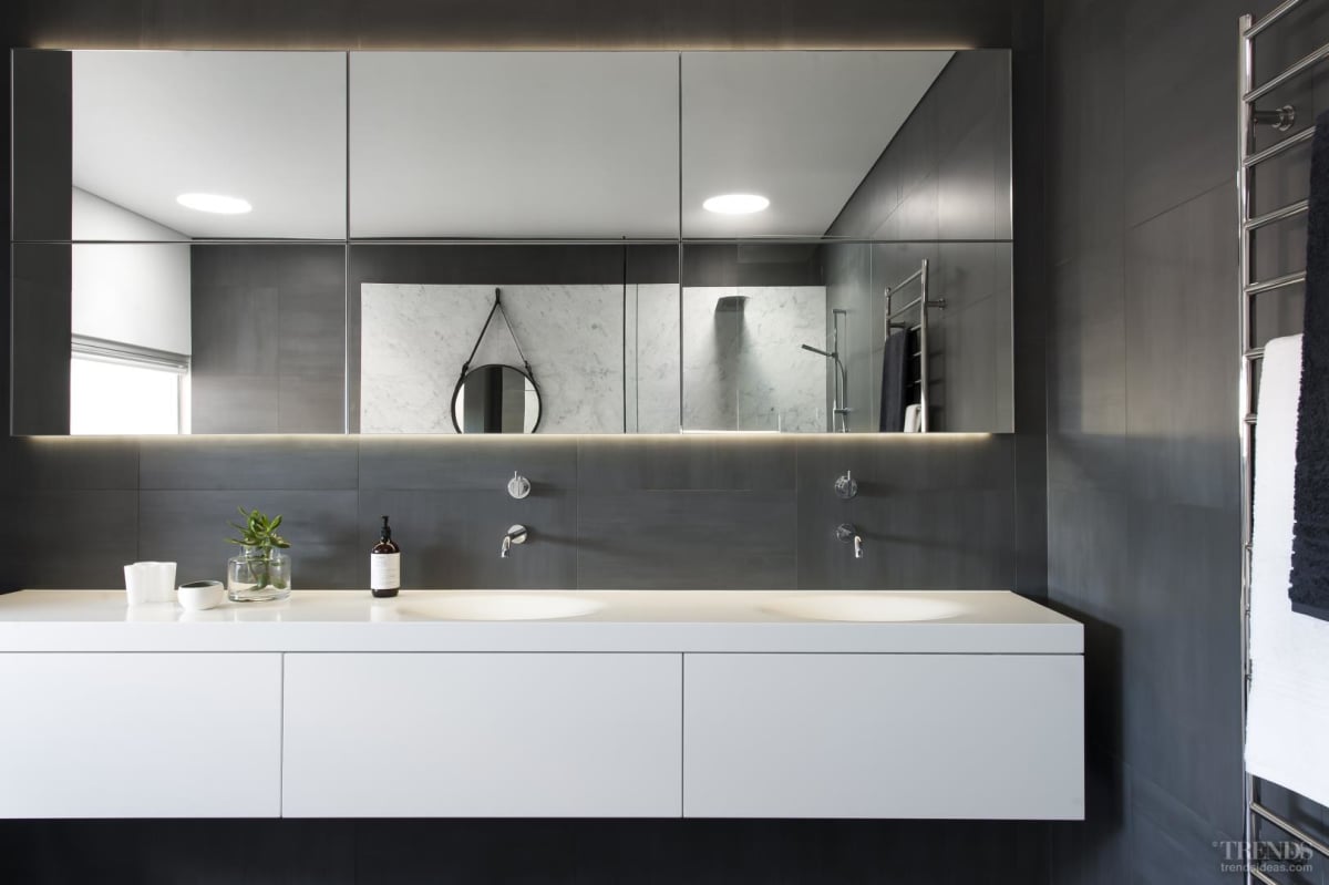 The hanging wall mirror and sky tube seen in reflection together with selected tapware introduce a round accent that helps soften the overall clean-lined space. Room lighting is in the form of dimmable LED uplighting running above the marble wall and the recessed mirror cabinets.